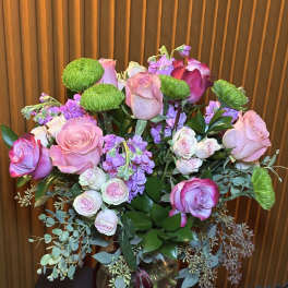 Pink and lavender roses in a glass vase with green button mums