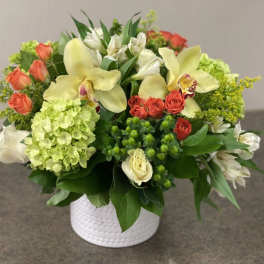 Mixed bouquet in a white textured vase with pale yellow orchids and coral roses