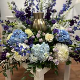 Blue hydrangeas, white chrysanthemums, and purple flowers in a gold vase