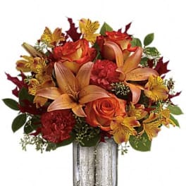 Orange roses and lilies in a silver vase with autumn-colored accents
