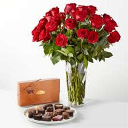 Red roses in a clear vase with a box of chocolates and a plate of candies