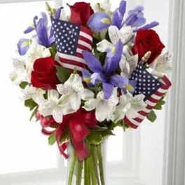 Red, white, and blue bouquet in a glass vase with small American flags