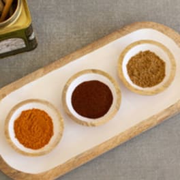 Wooden tray with three small bowls of spices and wooden spoons