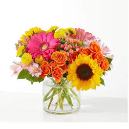 Colorful bouquet of gerbera daisies, roses, and sunflowers in a clear glass vase