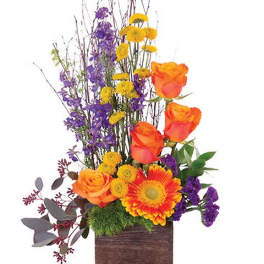 Orange roses and a gerbera daisy in a wooden box with purple and yellow flowers