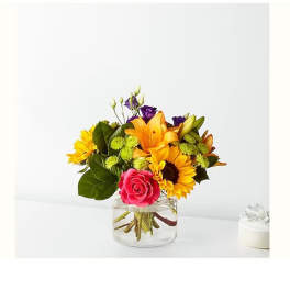 Bouquet of orange lilies, sunflowers, and a pink rose in a clear glass vase.