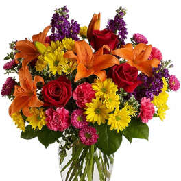 Bouquet of orange lilies, red roses, and yellow daisies in a clear glass vase