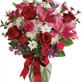 Bouquet of red roses, pink lilies, and white daisies in a glass vase