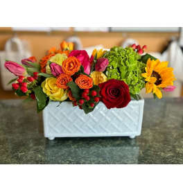 Mixed bouquet in a white rectangular vase with roses, tulips, and a sunflower