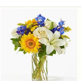 Bouquet of yellow sunflowers, white lilies, and blue flowers in a glass vase