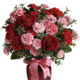 Red roses and pink carnations in a red glass vase with a pink ribbon