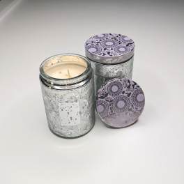 Two glass jar candles with patterned lids on a white surface