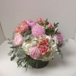 Low arrangement of pink peonies and roses with white hydrangeas in a clear glass vase
