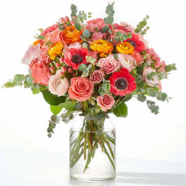 Bouquet of pink, coral, and yellow flowers in a clear glass vase