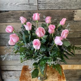 Pink roses arranged in a clear glass vase with greenery