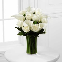 White calla lilies and roses arranged in a clear glass vase