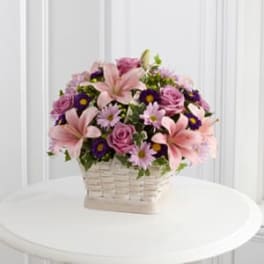 Pink lilies and roses in a white basket with purple daisies