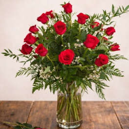 Red roses arranged in a clear glass vase with a matching rose on the table