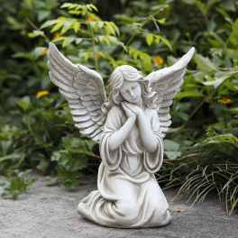 White angel statue kneeling with folded hands in a garden setting