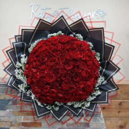 Large round bouquet of red roses with black wrapping and white filler flowers