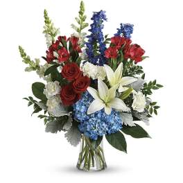 Bouquet of red roses, white lilies, blue hydrangeas, and red alstroemeria in a glass vase