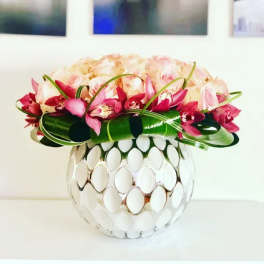 Pink and cream flowers arranged in a round mirrored vase