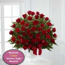 Red roses arranged in a white vase with a red ribbon