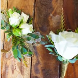 Two white rose bouquets with greenery and ribbon on a wooden surface