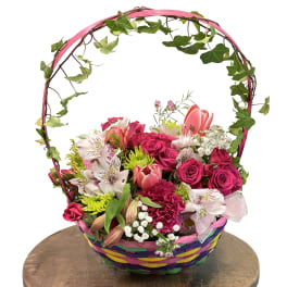 Basket arrangement of pink roses, tulips, and mixed flowers with an ivy handle