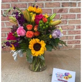Colorful mixed bouquet in a clear glass vase with sunflowers and roses