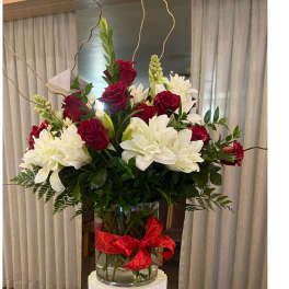Red roses and white lilies in a clear glass vase with a red ribbon