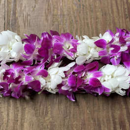 Two purple and white orchid leis on a wooden surface