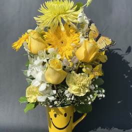 Yellow flower arrangement in a smiley-face mug with butterfly accents