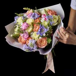 Hand-tied bouquet of pastel roses and purple blooms in white wrap
