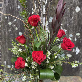 Red roses arranged with white filler flowers in a glass vase