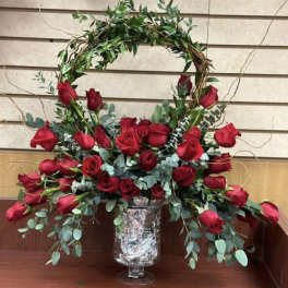 Red roses arranged in a tall vase with a leafy arch above
