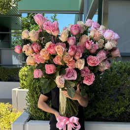 Large tall vase of pink and peach roses tied with a pink ribbon, held by a person outdoors