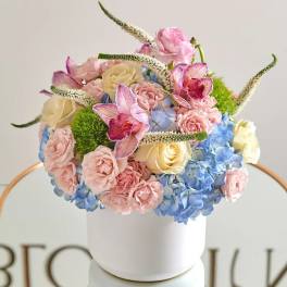 Pastel floral arrangement in a white cylindrical vase with roses and hydrangeas
