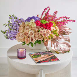 Mixed bouquet of roses and purple flowers in a white vase with a candle