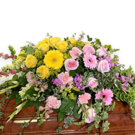 Casket spray with yellow and pink flowers and trailing greenery