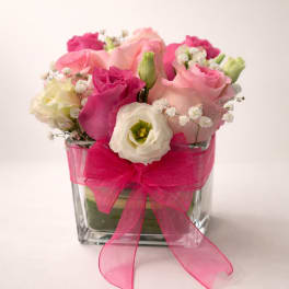 Pink and white roses arranged in a clear glass vase with a bright pink bow