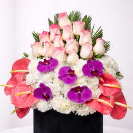 Pink-tipped roses, purple orchids, and white flowers in a black hat box