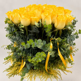 Yellow roses in a white vase with eucalyptus and yellow ribbon