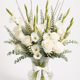 White roses and lilies in a clear glass vase with a white ribbon