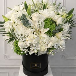 White floral arrangement in a black hat box with green accents