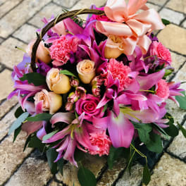 Basket arrangement of pink lilies, roses, and carnations with a satin bow