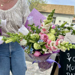Handheld bouquet of pink, white, and green flowers wrapped in purple paper