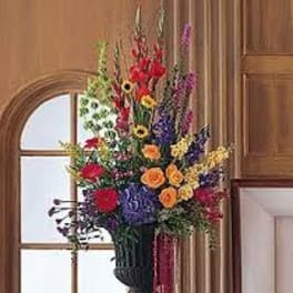 Tall mixed flower arrangement in a dark vase with red, yellow, purple, and orange blooms