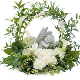 White roses and calla lilies arranged around a sleeping angel figurine