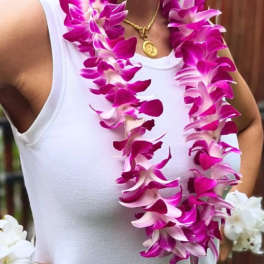 Woman wearing two magenta and white orchid leis over a white top.
